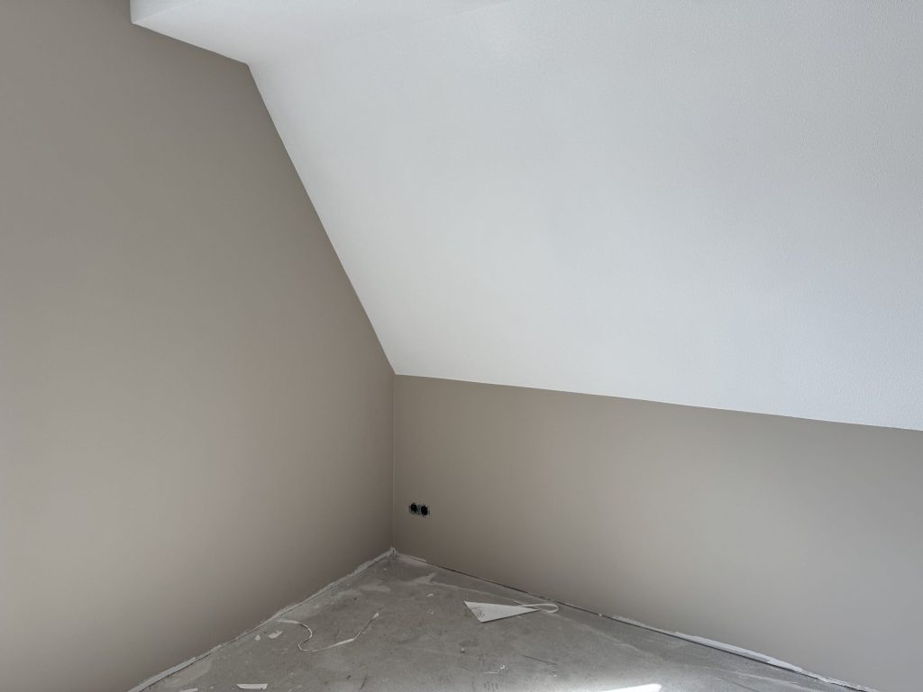 Zolderkamer met beige gesausde wanden onder een schuin wit plafond
