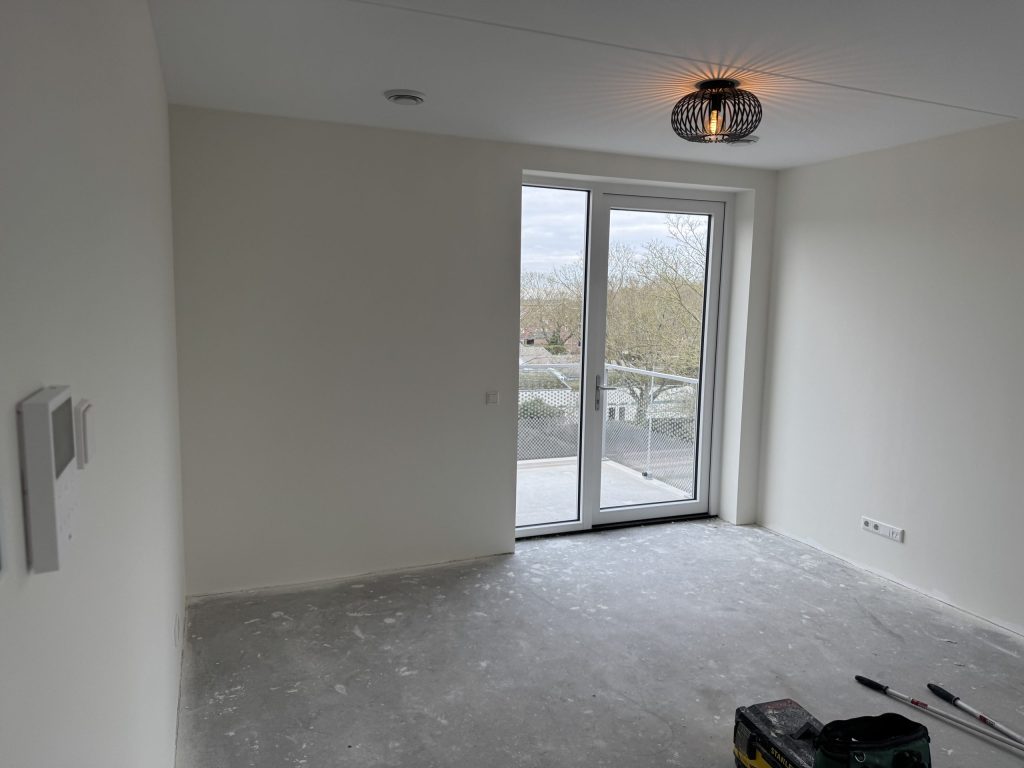Wit gesausde kamer in een nieuw appartement met openslaande deuren naar een balkon